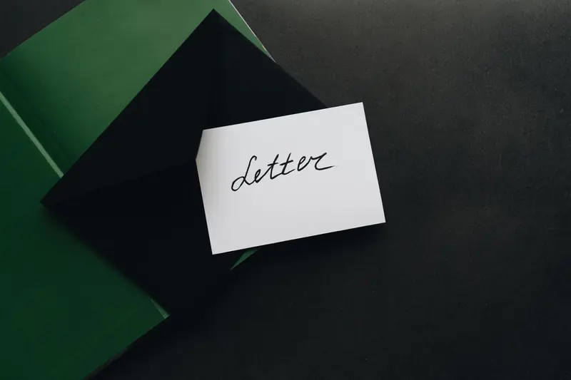 A flatlay showcasing a black envelope with a calligraphy letter, offering ample copyspace on a dark background