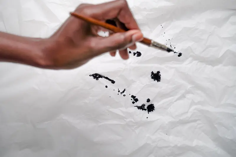 Close-up of a hand painting black ink strokes on crumpled white paper, showcasing creativity