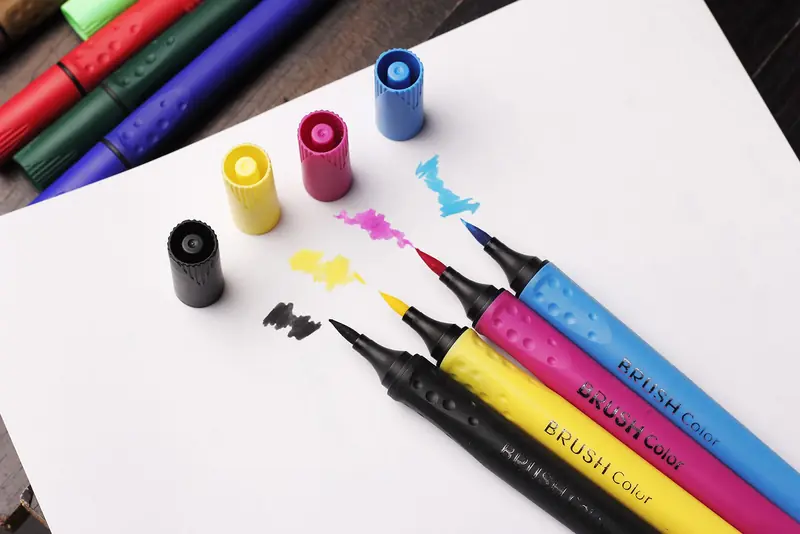 Top view of colorful brush markers with caps on white paper, perfect for art projects