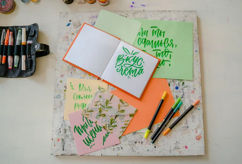 Flat lay of colorful calligraphy tools and artistic project on a desk