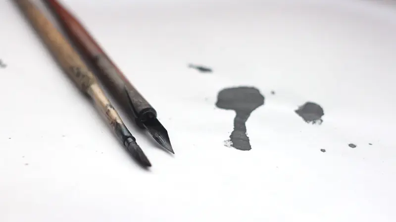 Close-up of calligraphy tools and ink spill on white surface, perfect for artistic themes