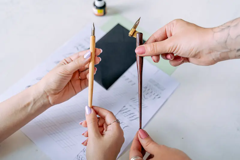 Close-up of hands holding calligraphy nib holders, emphasizing artistic focus