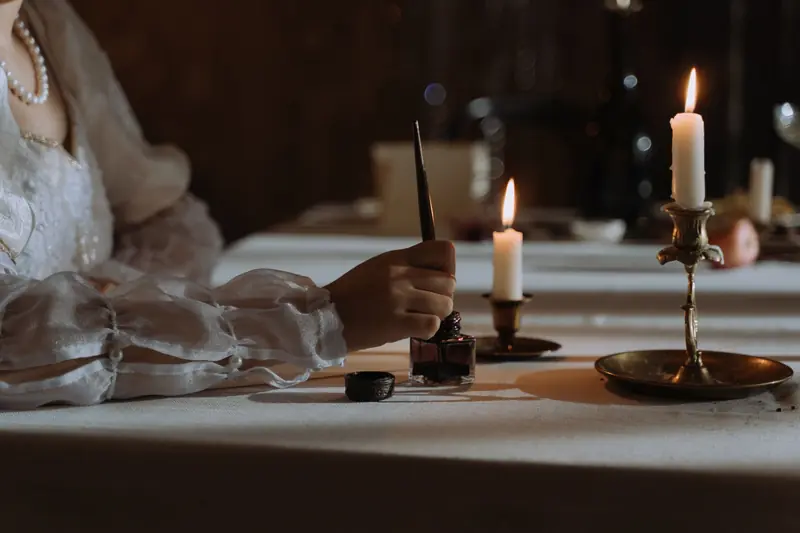 Atmospheric image of a hand writing with a quill by candlelight