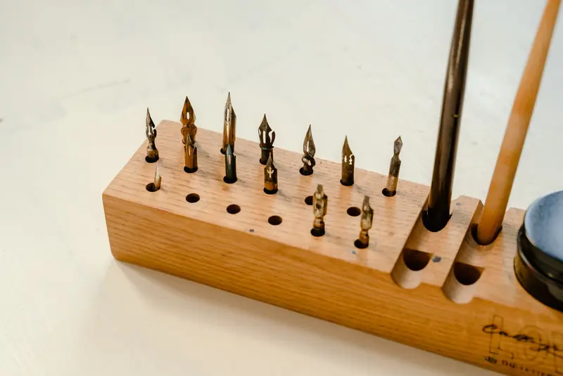 A wooden holder displaying various calligraphy nibs and tools for traditional handwriting art