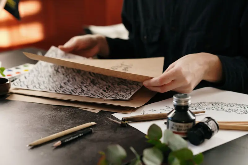 Close-up of calligraphy in progress with ink, pens, and paper on a desk. Art of hand lettering indoors