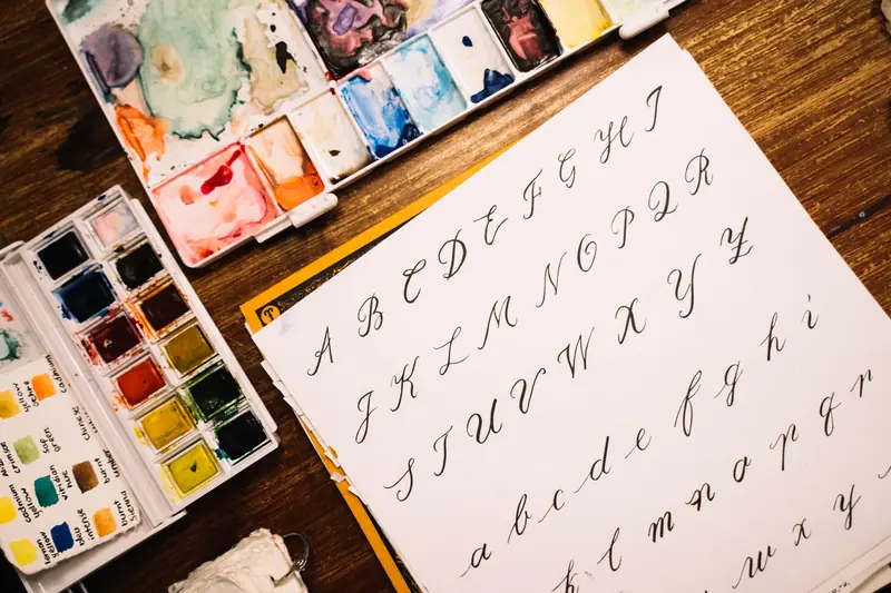 A flat lay of calligraphy letters alongside watercolor paints showcasing artistic tools and creative expression