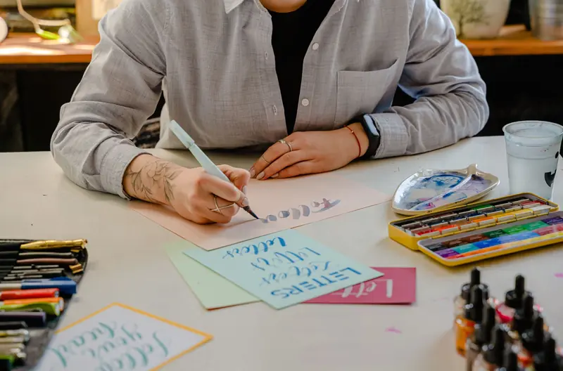 A person engaged in lettering with brush pens and inks on a desk