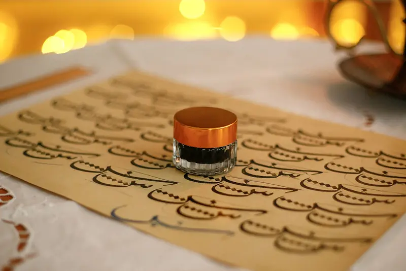 A beautifully arranged setup of Arabic calligraphy with an ink bottle on a bokeh background