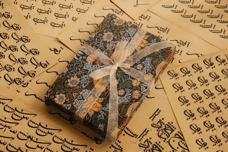 Elegant gift box wrapped with floral paper and ribbon on sheets of Arabic calligraphy