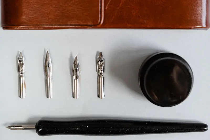 A flat lay of calligraphy nibs, holder, ink bottle, and leather case on a white background