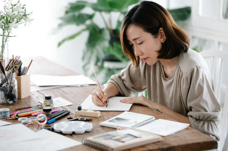 An adult woman artist engrossed in calligraphy work at a well-organized desk