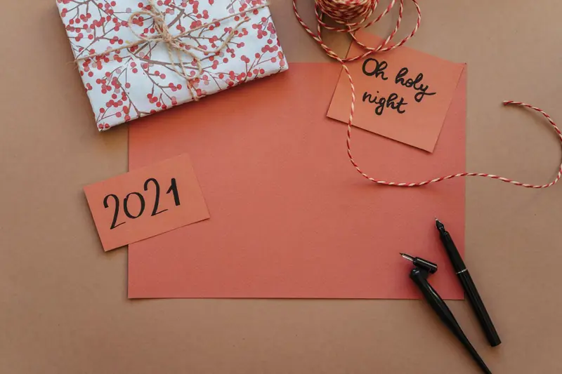 Top view of a holiday-themed stationery setup with gift box, handmade cards, and calligraphy pens