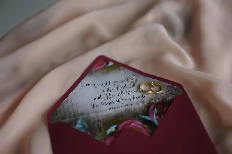 Close-up of a wedding invitation in a burgundy envelope with gold rings and a Psalm verse